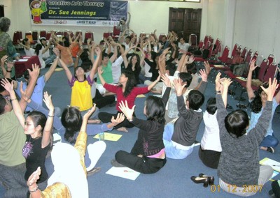 Sue facilitating a large group workshop, with participants raising their hands.