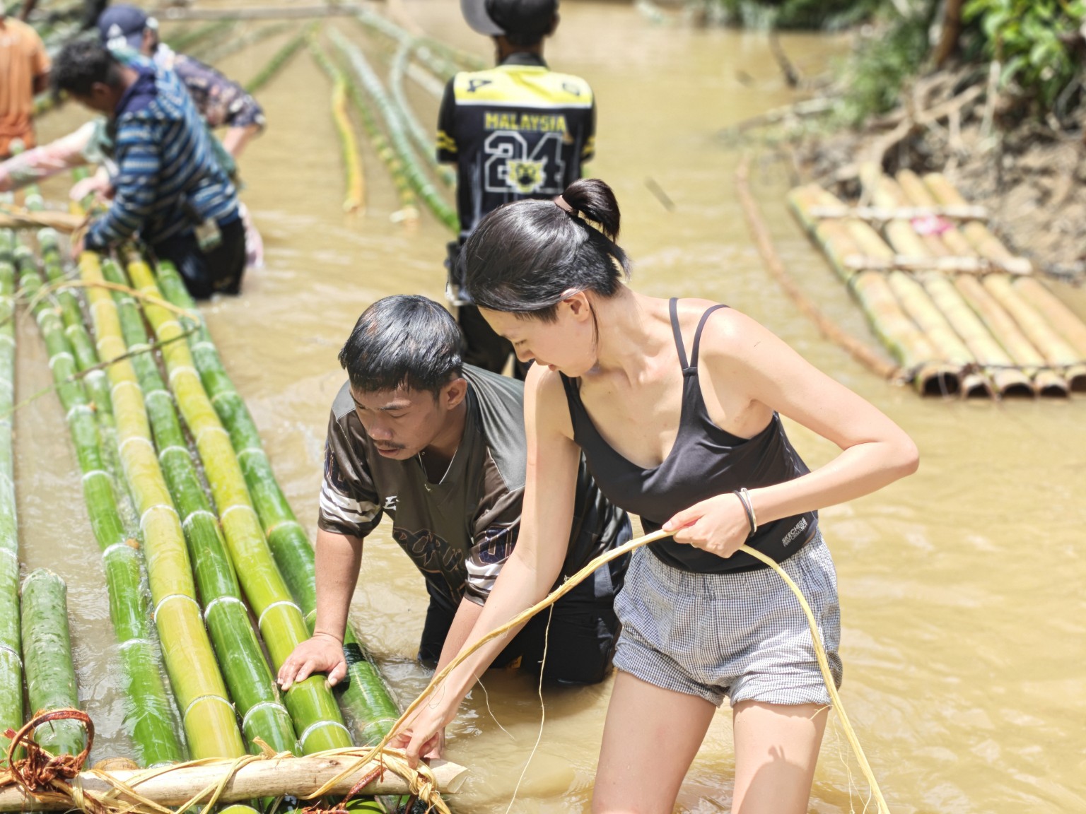 A Temiar man teaching an NDP student how to make a bamboo raft in a river in Kelantan in 2026