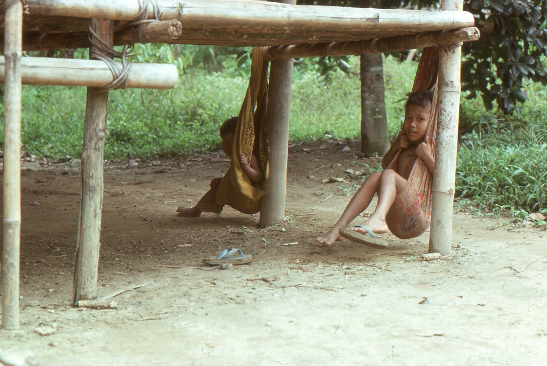 Two Temiar children resting in cloth hammocks beneath a raised wooden structure